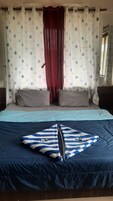 Una cama con una colcha azul y blanca a rayas, dos almohadas grises y una cortina roja.