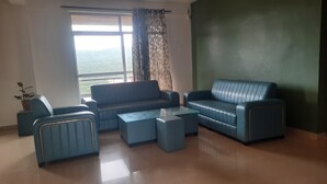 A living room with a sofa set, a coffee table, and a view through a window. - Bison Resort Amboli (Amboli)
