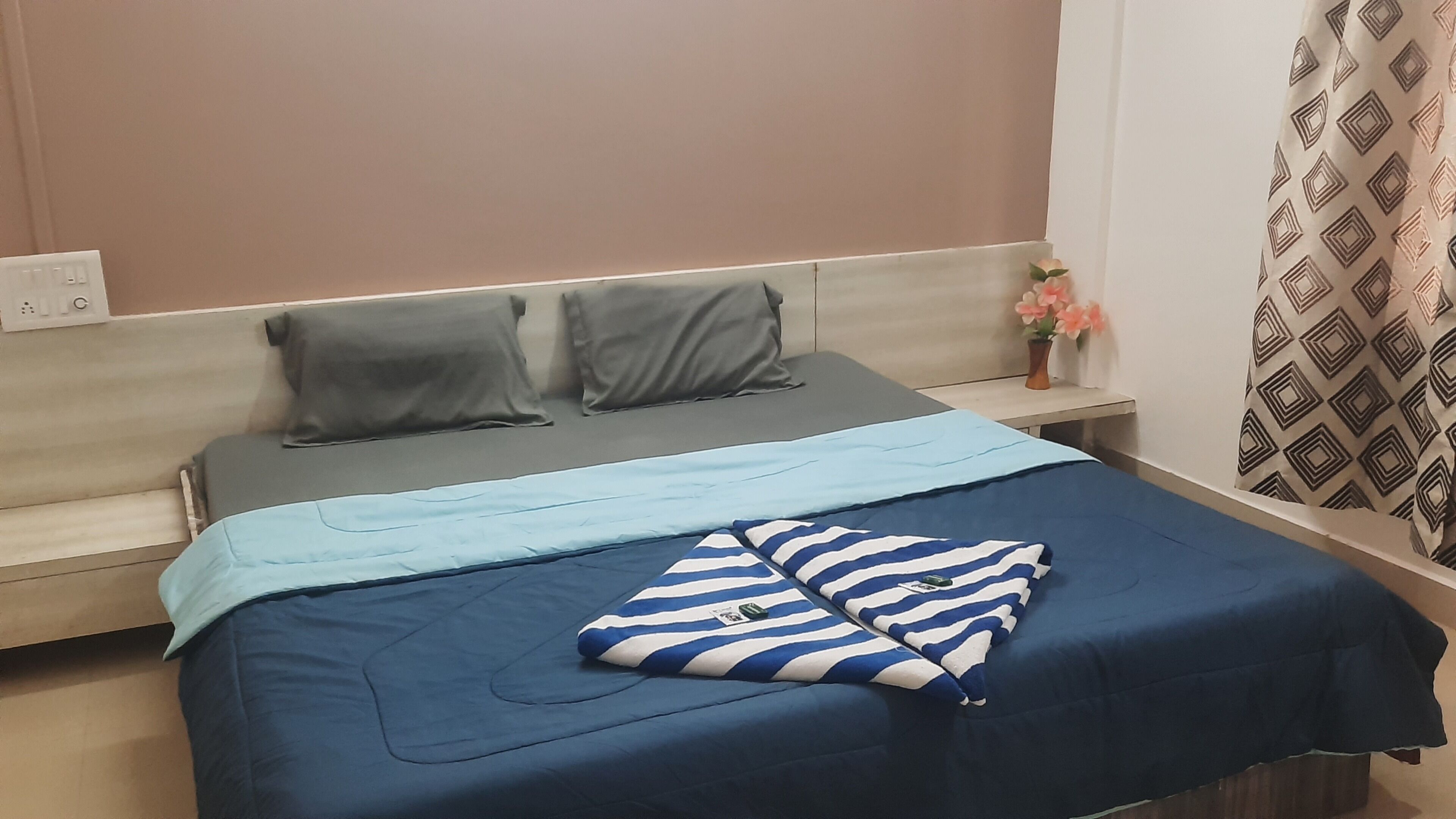 Una cama con un almohadón azul y blanco a rayas, un almohadón gris y una manta gris.