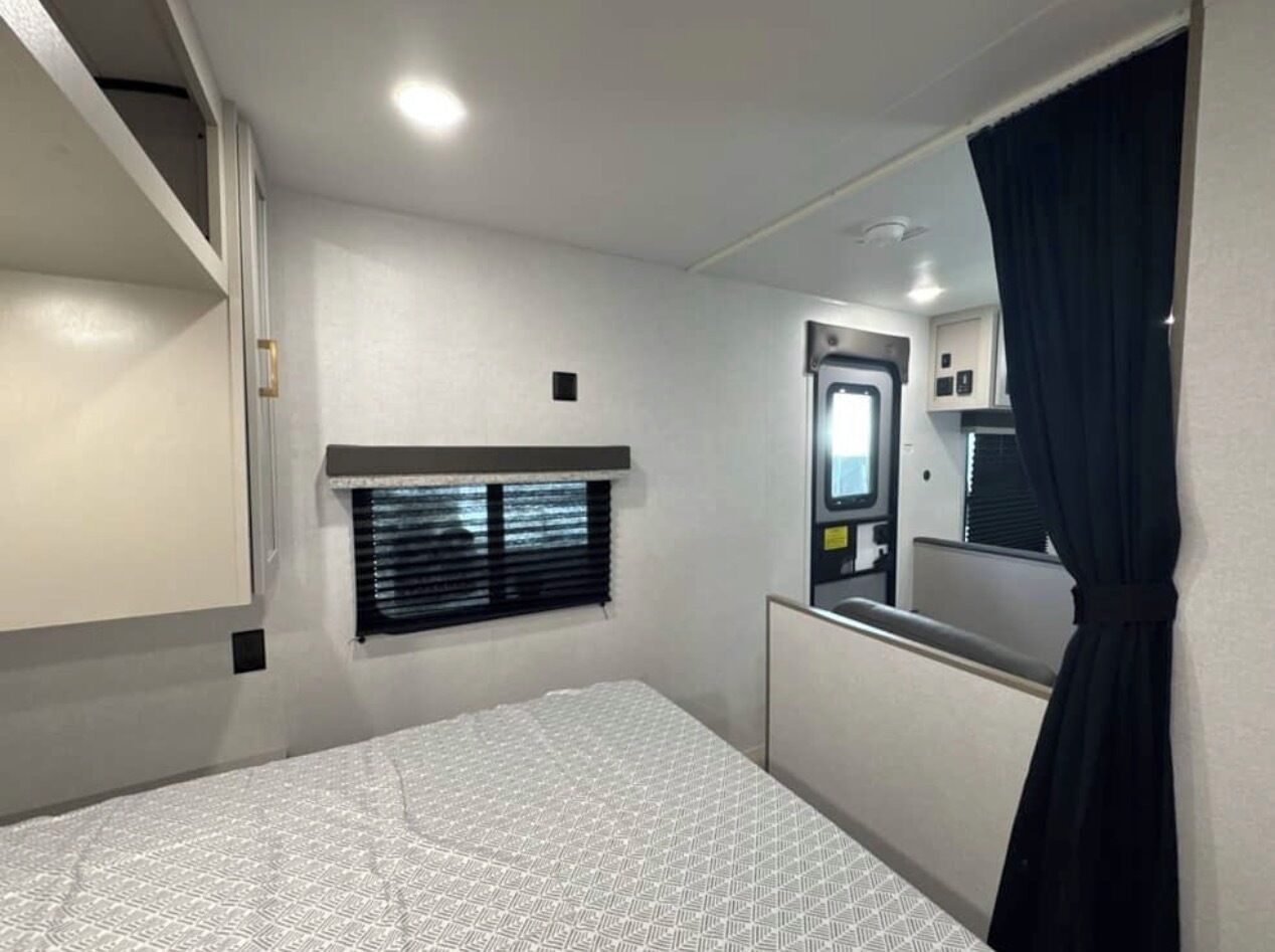 A bedroom with a bed, a window with blinds, a mirror, and a door.