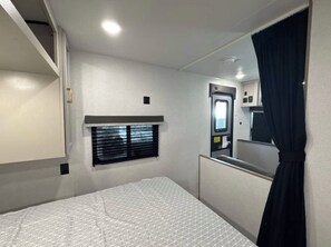 A bedroom with a bed, a window with blinds, a mirror, and a door.