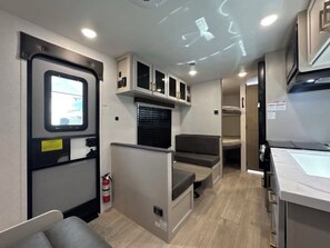 A compact RV interior with a kitchenette, seating area, and a small window.