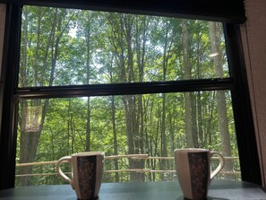 A window with a view of a forest through a bamboo railing.