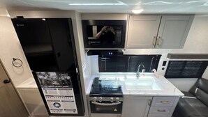 A compact kitchen with a built-in microwave, stove, and sink. - New RV camper in great nature,spring valley (Hamden)