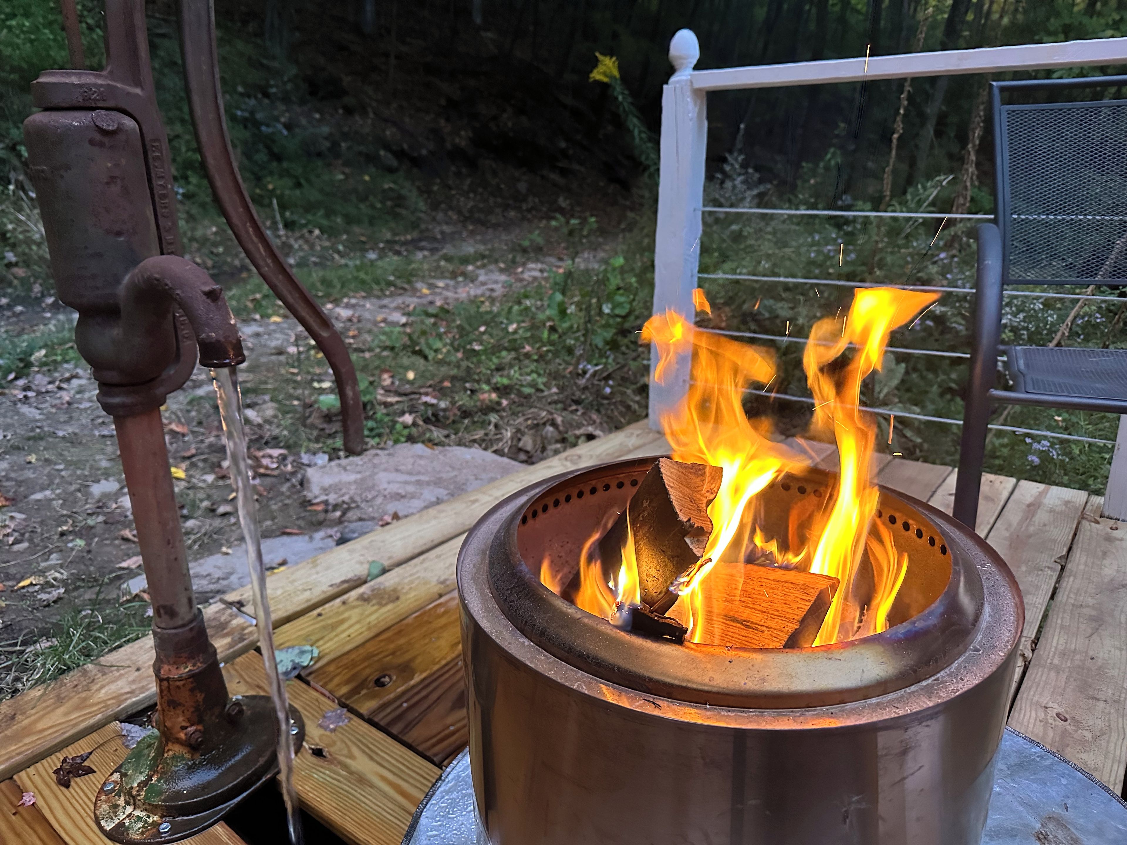 A metal fire pit with flames, a metal stand, and a wooden deck.