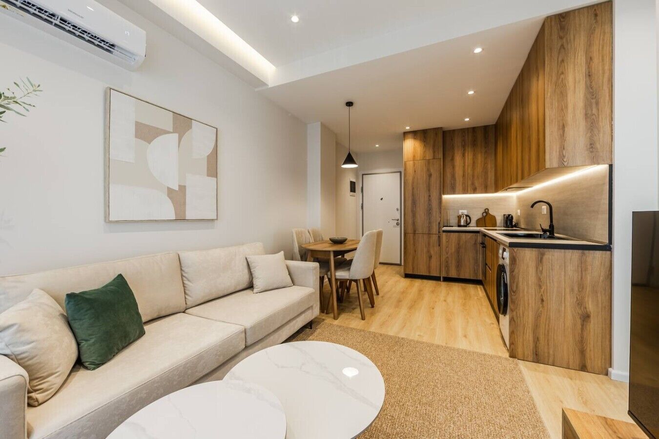 Een moderne woonkamer met een bank, een eettafel en een keukenhoek met houten kastjes.