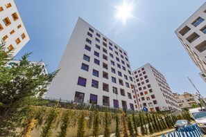 Un edifici modern i alt, amb múltiples pisos, envoltat de vegetació i un cel serè.