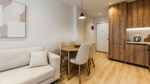 Un espacio habitable moderno con sofá, mesa de comedor, sillas y una zona de cocina con armarios de madera y una lámpara colgante.