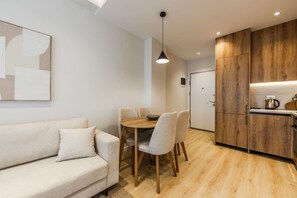 Un espacio habitable moderno con sofá, mesa de comedor, sillas y una zona de cocina con armarios de madera y una lámpara colgante.