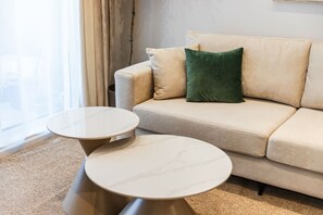 Un salón moderno con un sofá color beige, dos mesas redondas de mármol y un cojín verde decorativo.