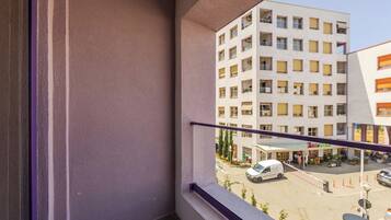 Ein Balkon mit Blick auf ein mehrstöckiges Gebäude, eine Straße mit parkenden Autos und eine kleine Außen-Sitzgelegenheit.