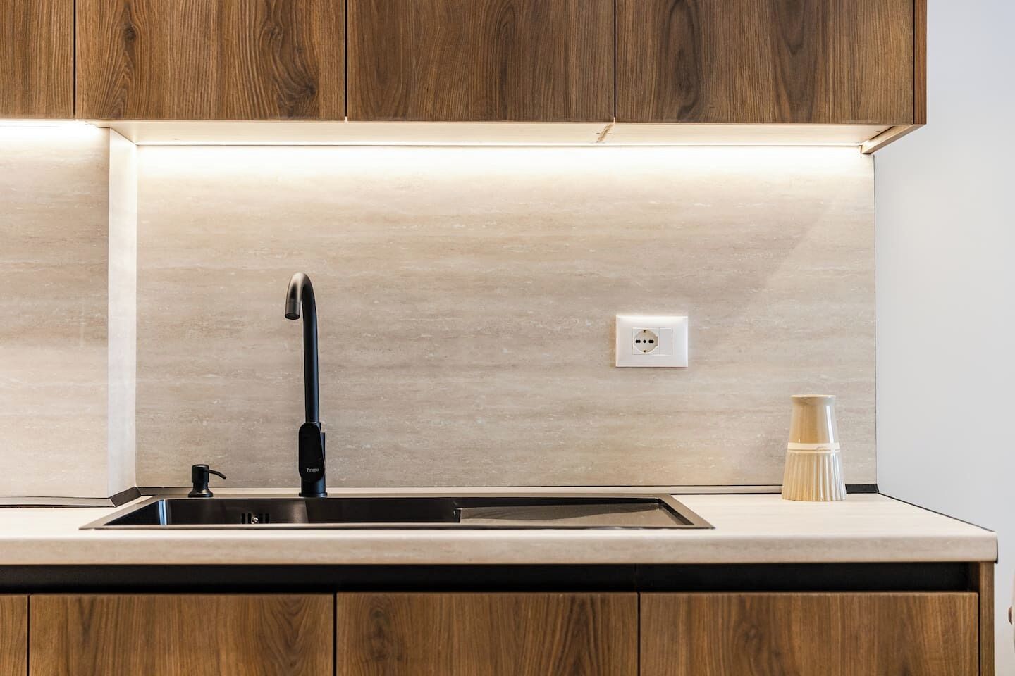 A kitchen with a modern faucet, a light switch, and a wooden cabinet.