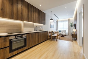 Una cocina moderna con armarios de madera, horno empotrado y comedor con mesa y sillas redondas.