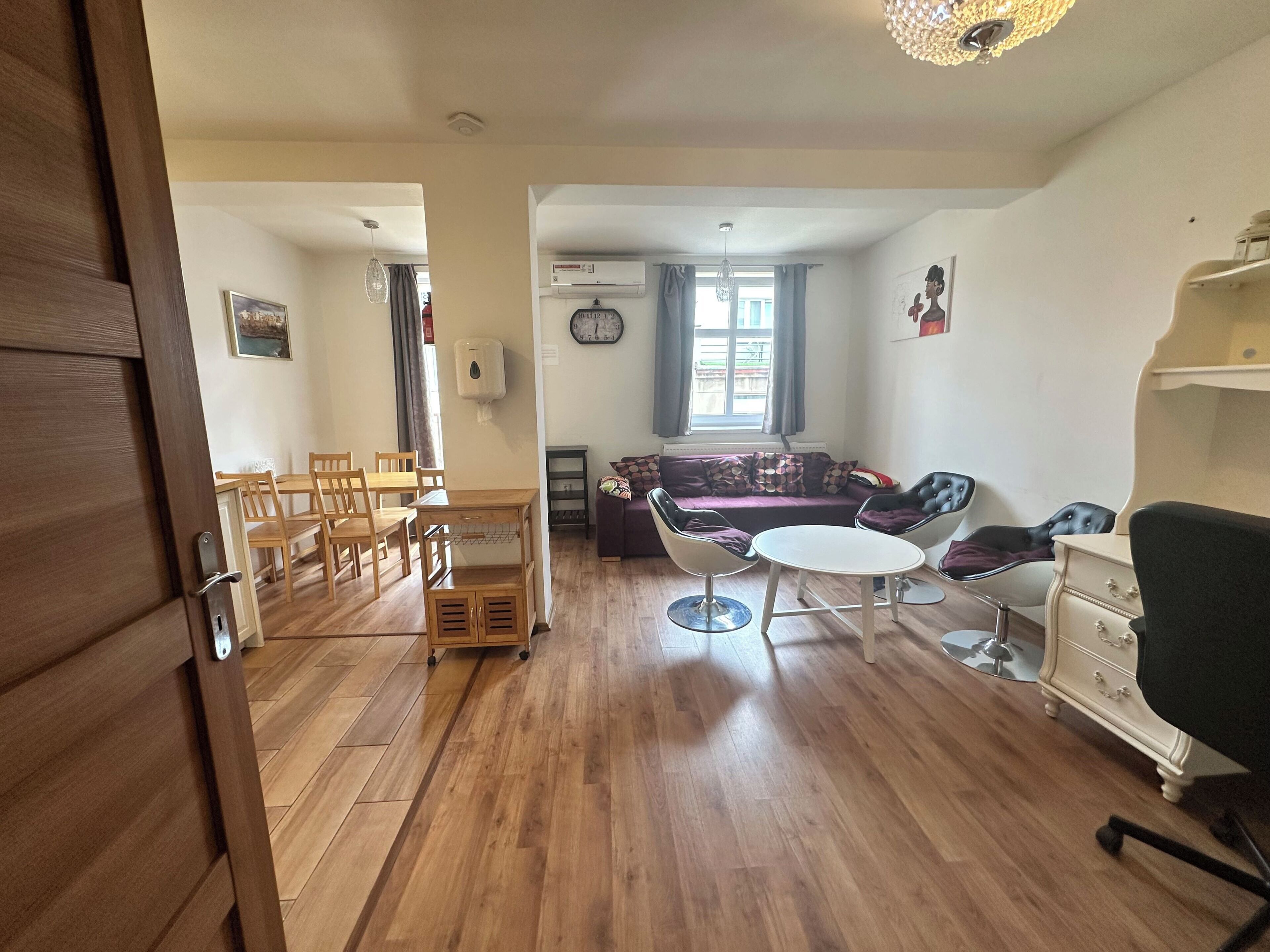 A living room with a wooden floor, a sofa, a coffee table, and a dining area with chairs and a table.