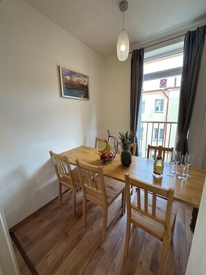 A dining area with a wooden table, chairs, a fruit basket, a pineapple, a bottle of champagne, and wine glasses. - Spacious Karlín 2BR+Living Room. Metro 1 Min. Elevator. (Hlavní město Praha)