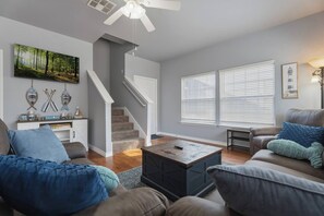 A living room with a staircase, a fireplace, and a large window with blinds. - Monkey Island Nautical Escape (Afton)