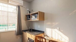 A compact kitchen with a sink, wooden cabinets, and a window with curtains. - Studio in Velha w/ City View Ola0002 (Blumenau)