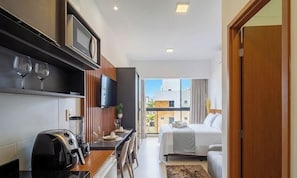 A modern hotel room with a kitchenette, a dining area, a bed, and a balcony with a city view. - Comfort in Condo With Pool and Gym Azz0402 (Cabedelo)