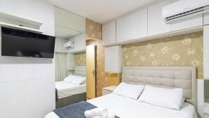 Una habitación de hotel con una cama, televisor, armario y equipo de aire acondicionado.