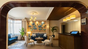 A hotel lobby with a reception desk, seating area with sofas, a coffee table, and a decorative wall with floral artwork.