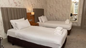Quarto de hotel com duas camas, uma mesa de cabeceira, uma luminária e um espelho.