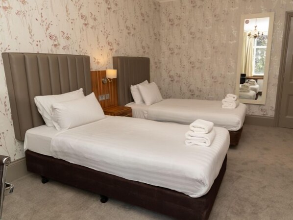 Una habitación de hotel con dos camas, una mesita de noche, una lámpara y un espejo.