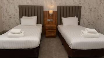 A hotel room with two beds, a wooden nightstand, and a wall-mounted lamp.
