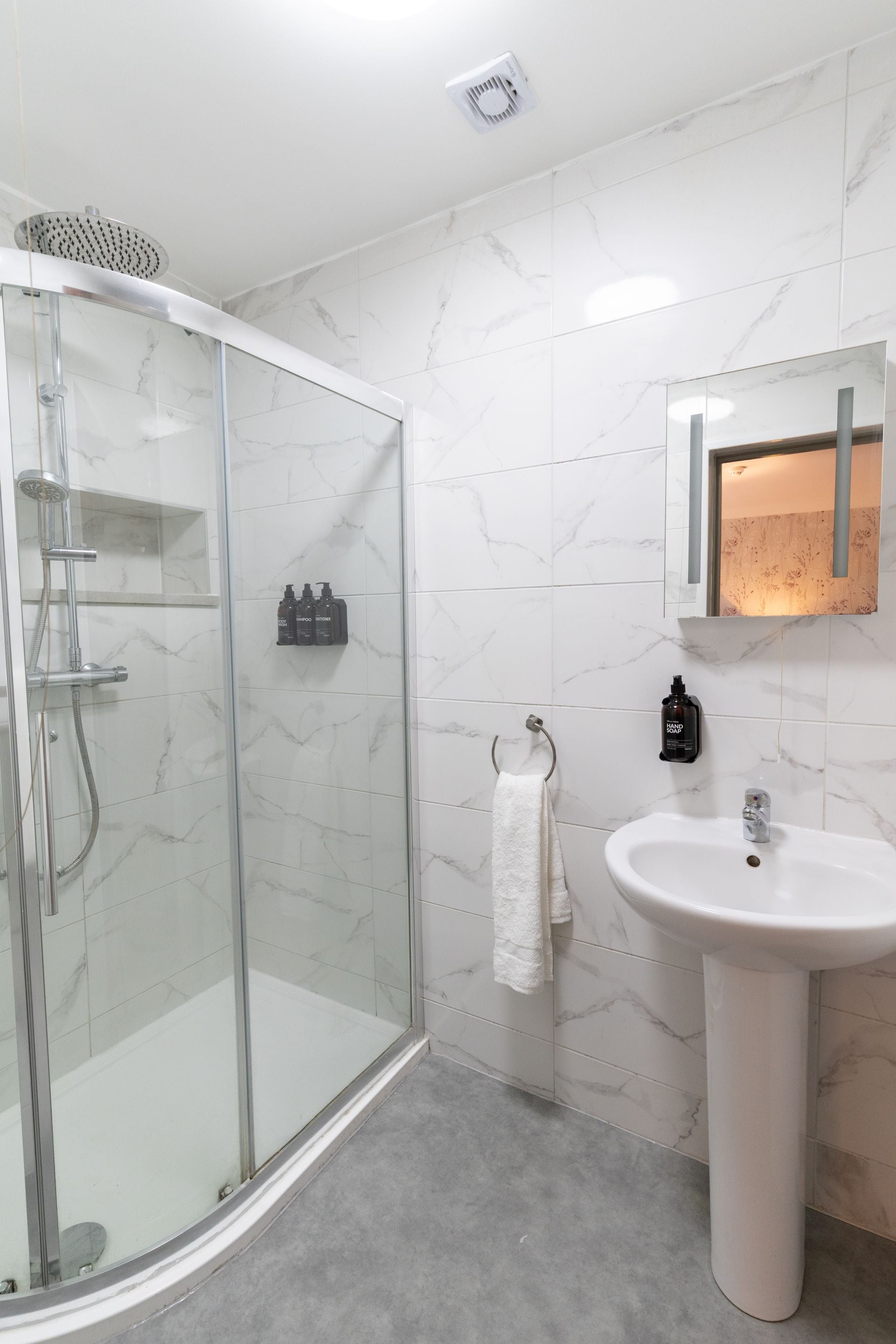 Une salle de bain moderne avec une douche à parois de verre, un lavabo blanc et un miroir avec éclairage intégré.