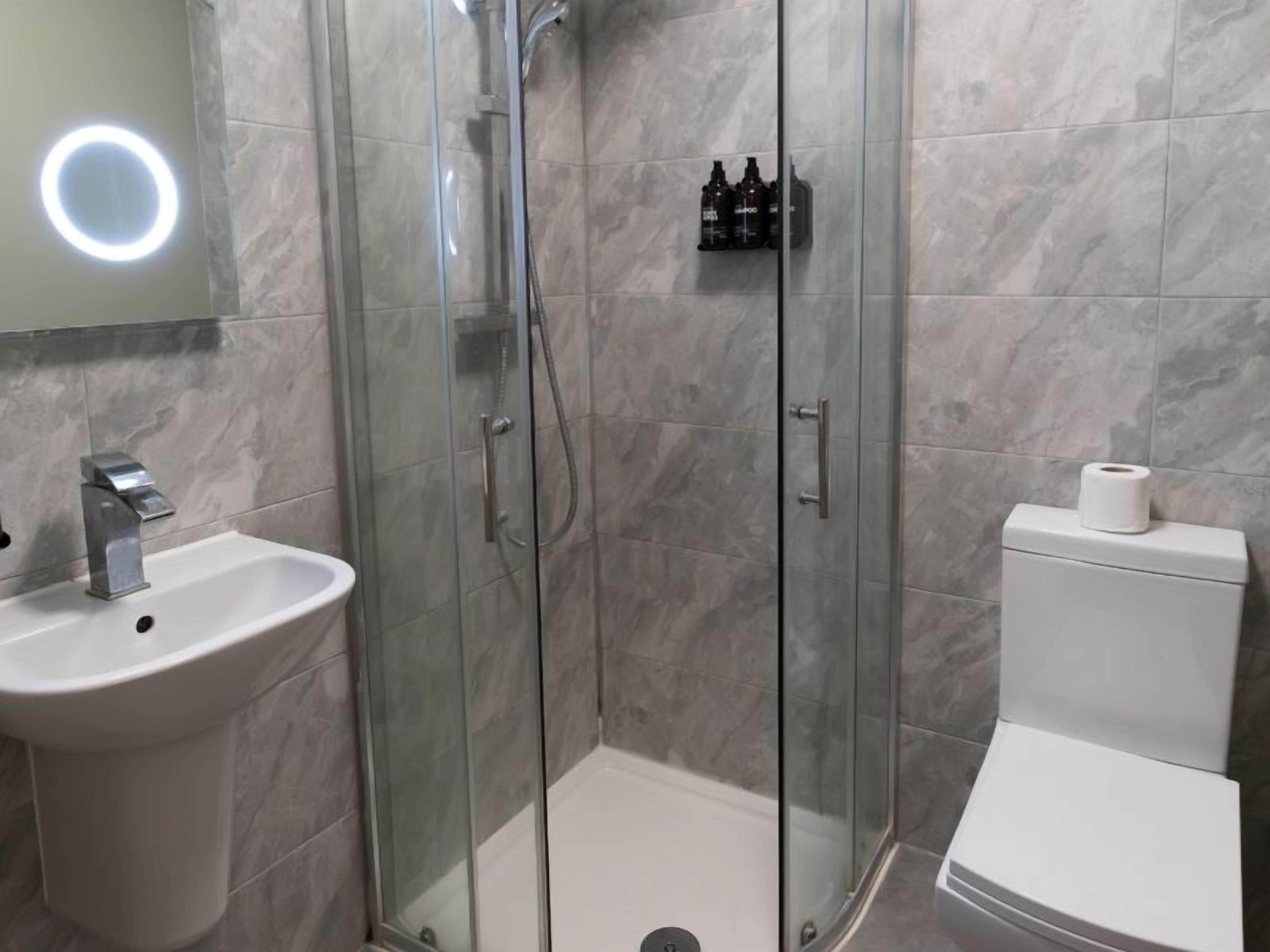Kylpyhuone, jossa on lasiseinällä varustettu suihku, pesuallas ja wc.