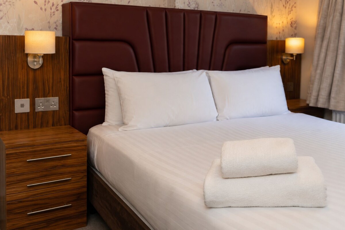 A hotel room with a large bed, two bedside tables, and wall-mounted lamps.