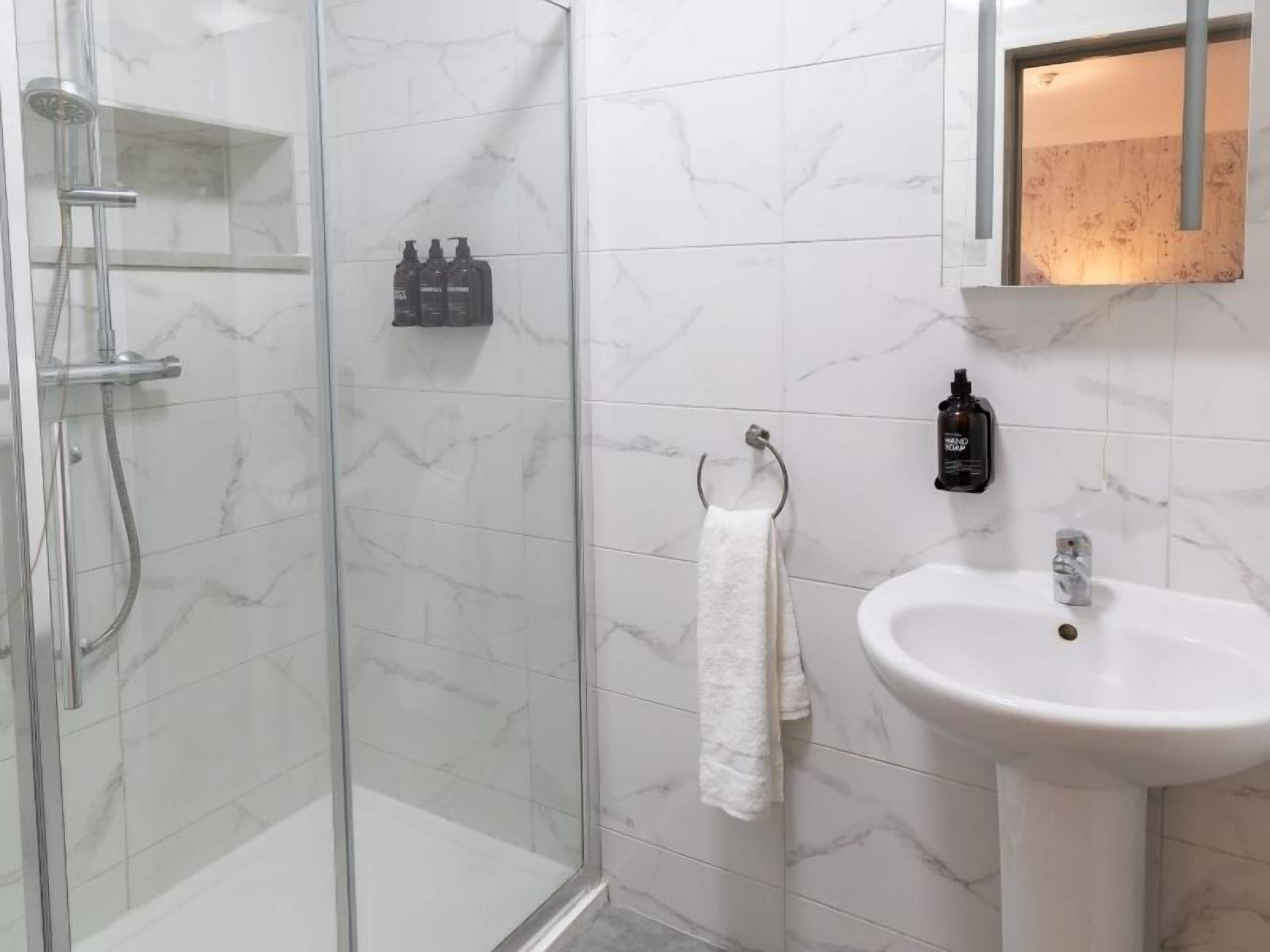 A bathroom with a glass shower enclosure, a white sink, and a mirror.