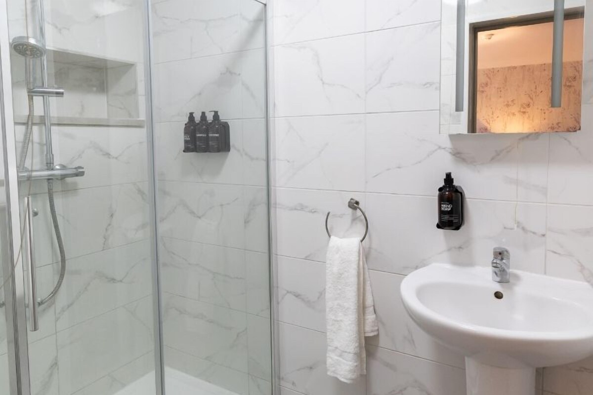 A bathroom with a glass shower enclosure, a white sink, and a mirror.