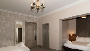 A hotel room with two beds, a large mirror, a chandelier, and a door leading to another room.