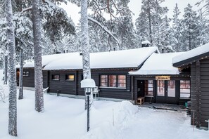Una cabaña de madera con techo cubierto de nieve, rodeada de árboles.