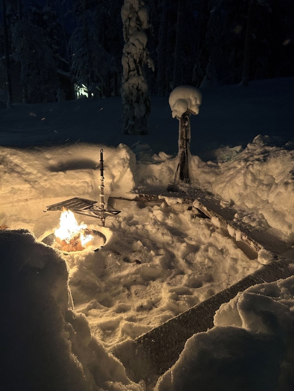 A snow-covered outdoor area with a fire pit and a metal structure, possibly a grill or barbecue.