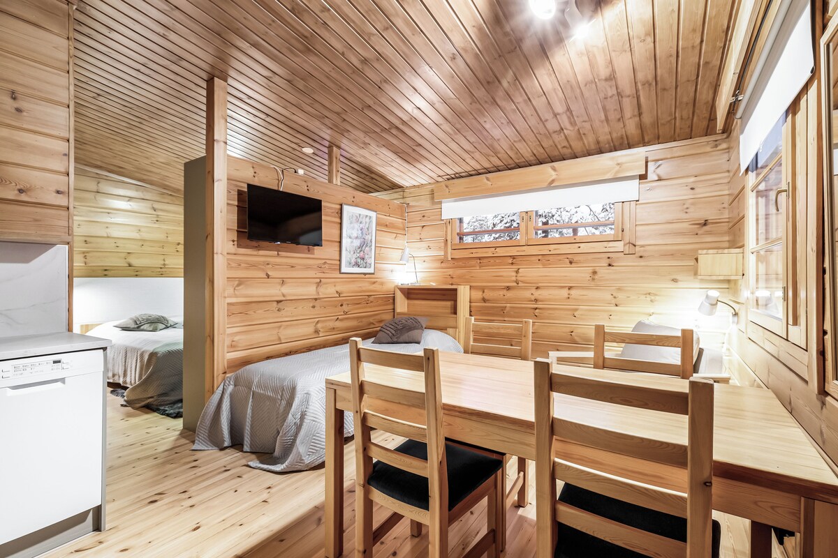 L’intérieur d’un chalet en bois comprend un lit, une table à manger, des chaises, un téléviseur et une fenêtre.