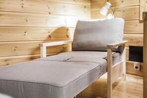Un lit simple avec un matelas et un oreiller gris, dans une pièce en bois, avec une lampe de chevet.