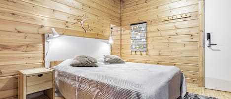 A wooden-paneled room with a bed, bedside table, lamp, and a wall-mounted artwork.