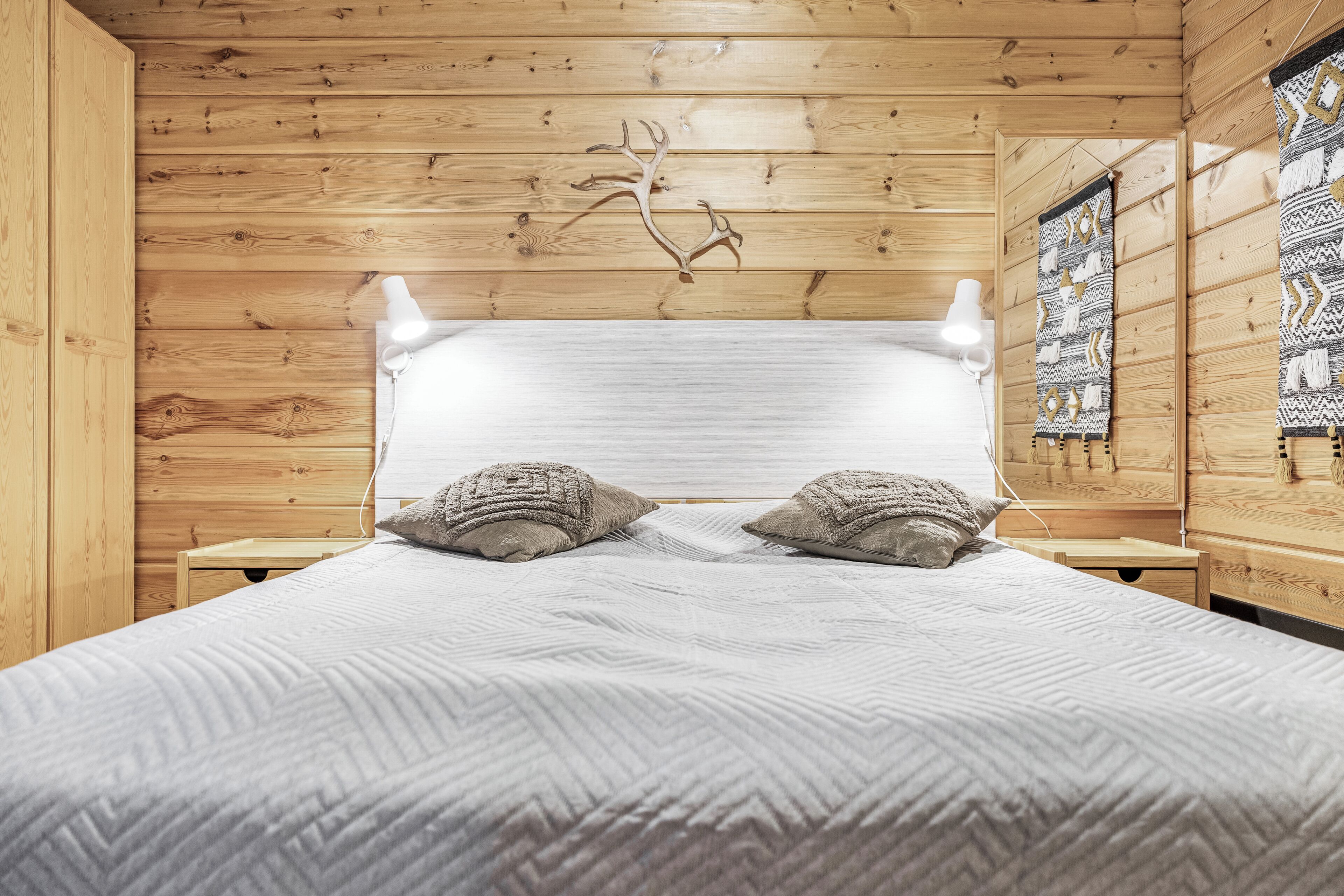 Una habitación con piso de madera, una cama, dos mesitas de noche y un tapiz decorativo en la pared.
