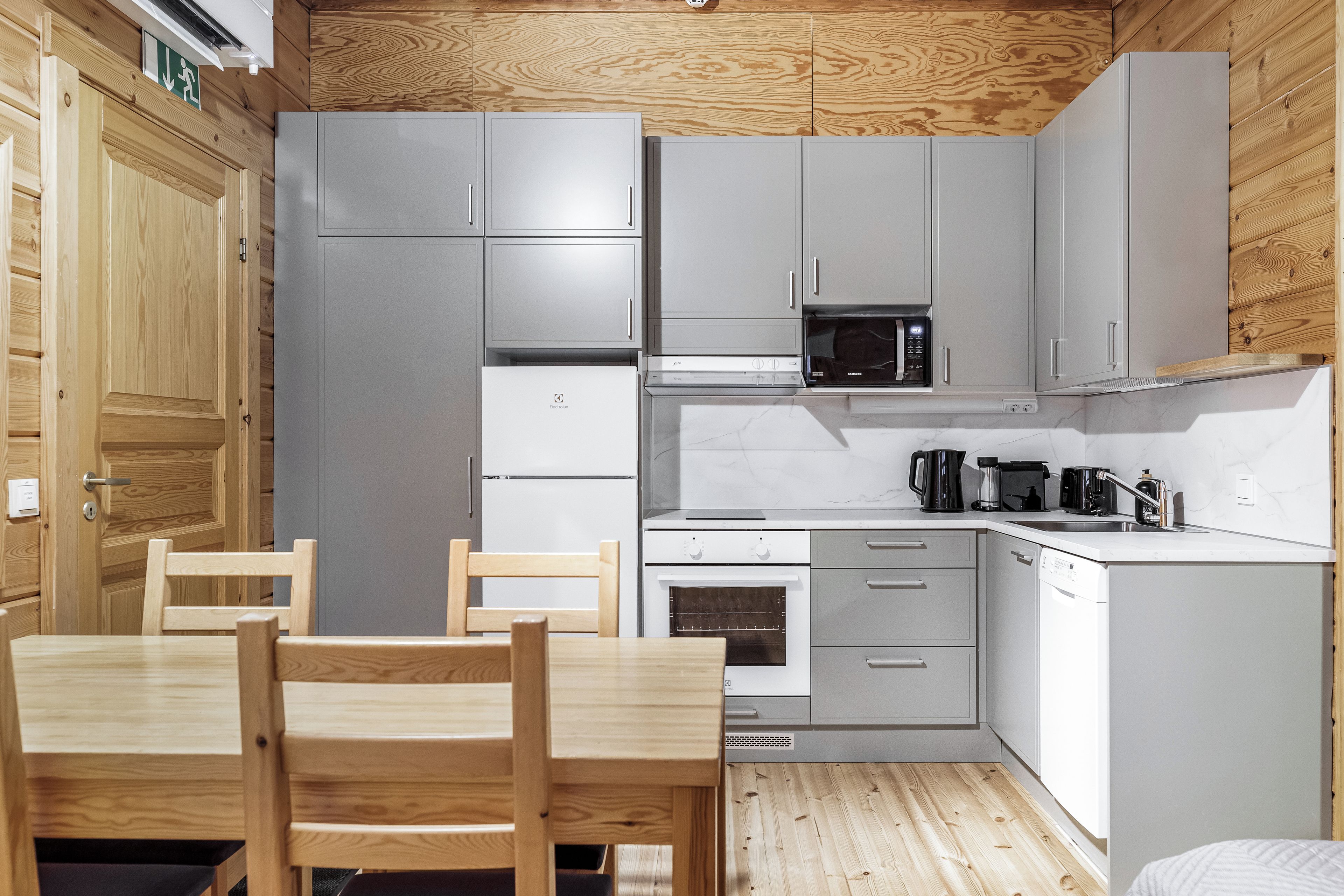A compact kitchen with grey cabinets, a microwave, a stove, and a sink. There is a wooden dining table with chairs.