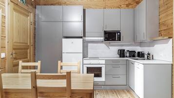 A compact kitchen with grey cabinets, a microwave, a stove, and a sink. There is a wooden dining table with chairs.
