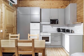 Une cuisine compacte avec des meubles gris, un four à micro-ondes, une cuisinière et un évier. On y trouve une table à manger en bois avec des chaises.
