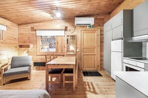 A compact wooden cabin interior with a dining area, kitchenette, and a window with a view of snow-covered trees.