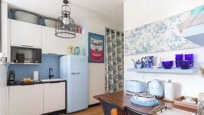 A modern kitchen with white cabinets, a blue refrigerator, and a dining area with a wooden table and chairs. - Apartment in the Heart of Deauville With a Garden (Deauville)