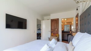 A hotel room with a bed, a flat-screen TV mounted on the wall, a wooden door, a mirror, and a small table with a chair. - Apartment in the Heart of Deauville With a Garden (Deauville)