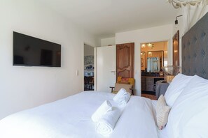 A hotel room with a bed, a flat-screen TV mounted on the wall, a wooden door, a mirror, and a small table with a chair. - Apartment in the Heart of Deauville With a Garden (Deauville)