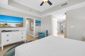 A bedroom with a large bed, a dresser, a mirror, and a painting of a beach scene. - Sterling Breeze 507- Dancing Waves (Panama City Beach)
