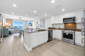 A modern kitchen with white cabinetry, a granite countertop, stainless steel appliances, and a view to the outside. - Sterling Breeze 507- Dancing Waves (Panama City Beach)