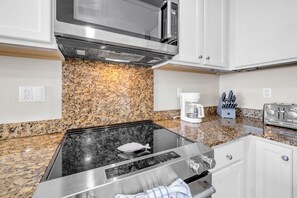 A modern kitchen with a granite countertop, stainless steel appliances, and white cabinetry. - Sterling Breeze 507- Dancing Waves (Panama City Beach)