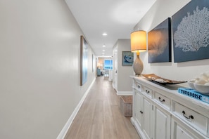 A hallway with a wooden floor, white walls, and a white cabinet with drawers. - Sterling Breeze 507- Dancing Waves (Panama City Beach)